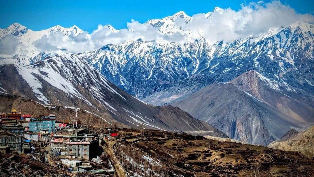 A mountainous landscape with snow-capped peaks, a village with colorful buildings, and a clear blue sky. 1
