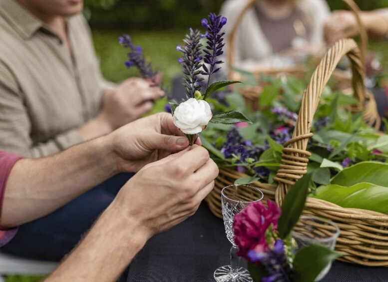 A person placing a white flower on a table with a glass and a basket of flowers. 5