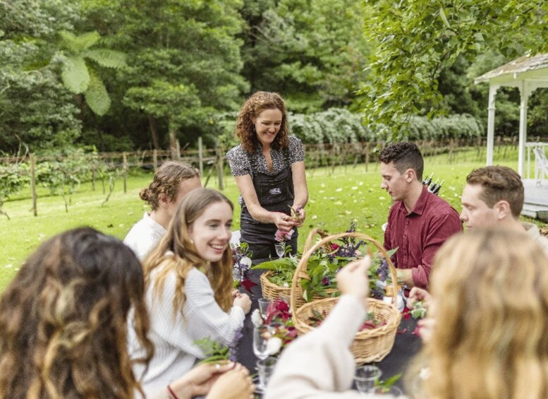 A group of people seated around a table with baskets of flowers and a white gazebo in the background. 3