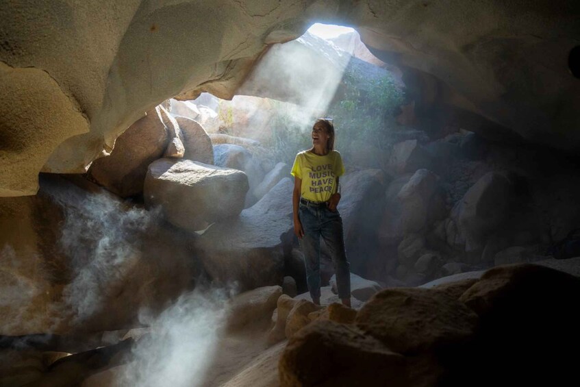 Une personne se tient dans une grotte, entourée de gros rochers et de vapeur. 1