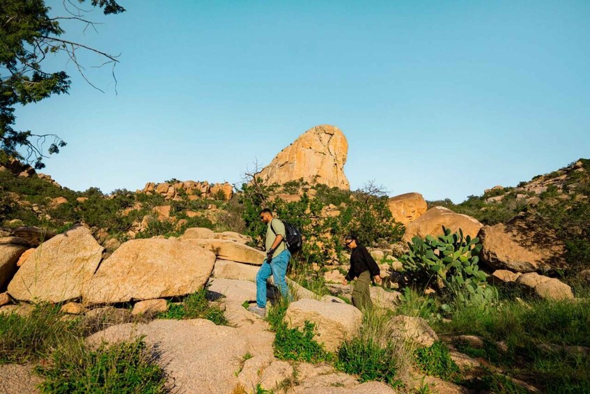 Two people hiking on rocky terrain with a large rock formation in the background. 3