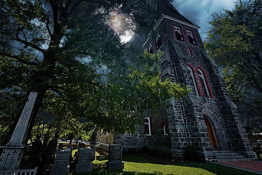 A Gothic-style church with a tall tower, surrounded by trees and a cemetery with headstones. 1
