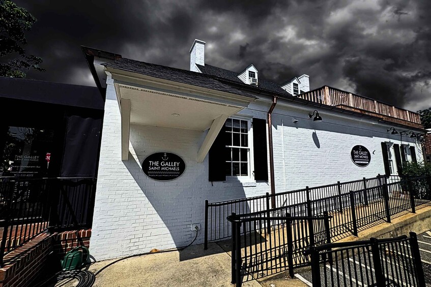 A white building with black shutters and a black metal fence in front. There are two signs on the building that read 'The Galley Saint Michaels'. 4