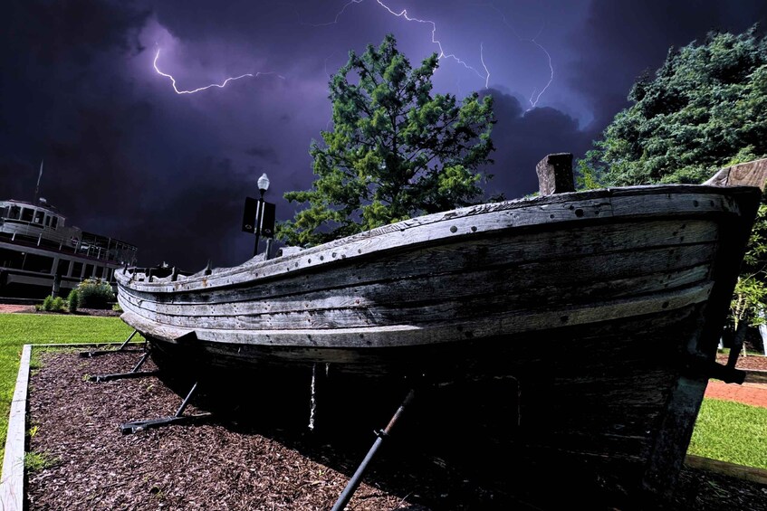 Un vieux bateau en bois, usé par les éléments, est exposé, et l’on aperçoit des éclairs dans le ciel en arrière-plan. 5