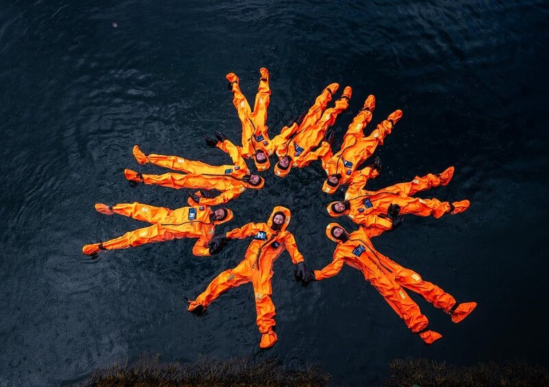 Eine Gruppe von Menschen in orangenen Anzügen, die in einer kreisförmigen Formation im Wasser schweben. 1