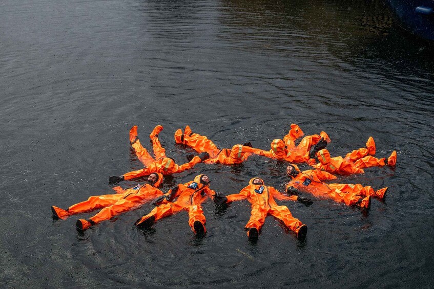 Eine Gruppe von Personen in orangefarbenen Schutzkitteln, die auf dem Wasser treiben. 3