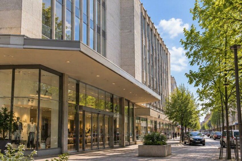 A modern building with large glass windows, a paved sidewalk, and a street with cars and trees. 3