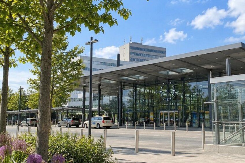 A modern building with a glass facade, a clock, and a parking area with cars. 2