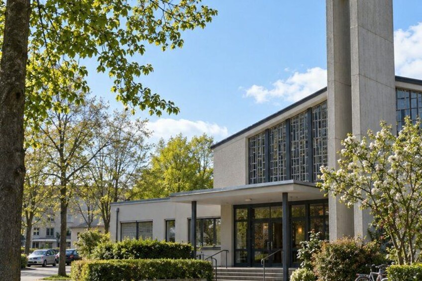 A modern building with large windows, a covered entrance, and a tree-lined pathway. 5