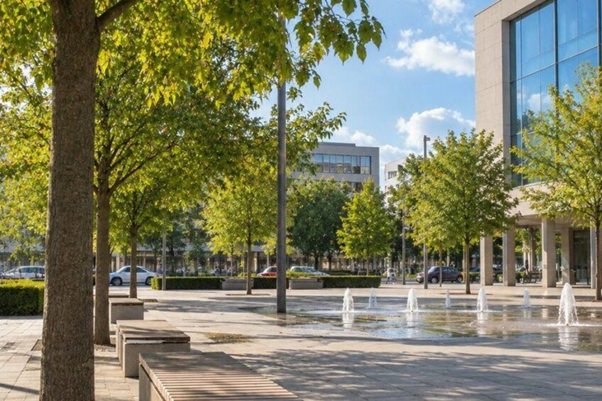 A modern building with a glass facade, a tree-lined pathway, and a water feature. 4