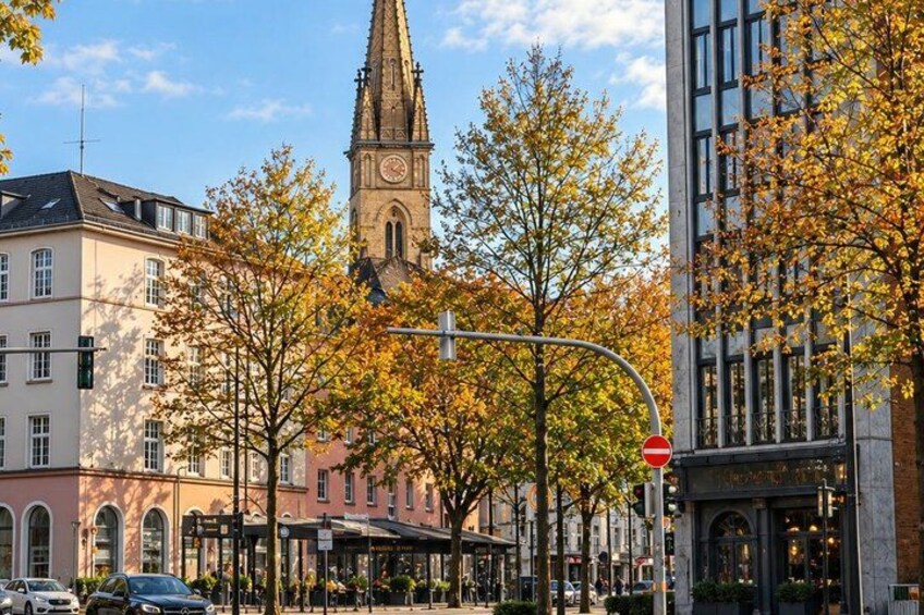 A city street with autumn trees, a church tower, and modern buildings. 5
