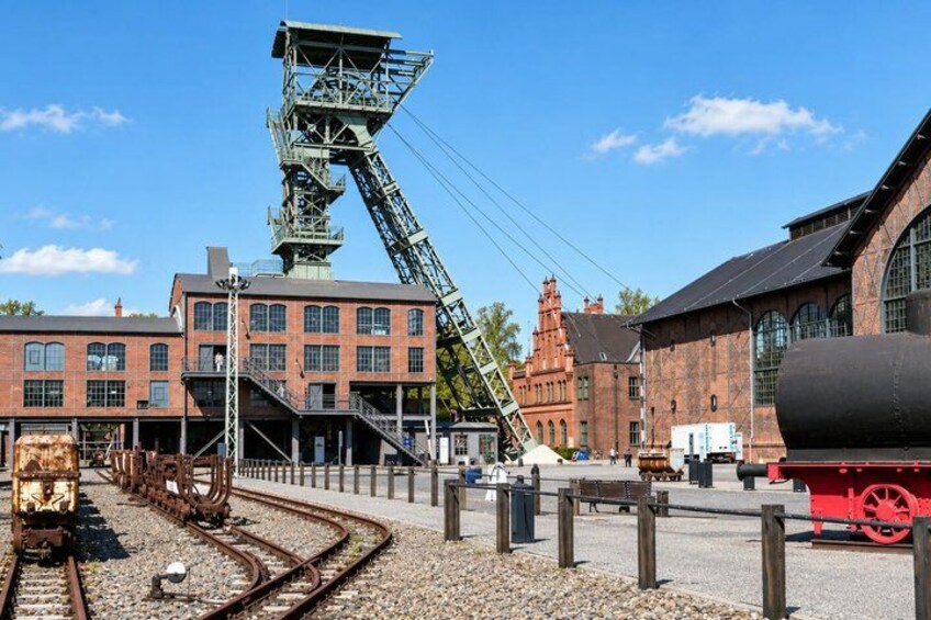 A historic industrial site with a large mining tower, railway tracks, and a large cylindrical tank. 4