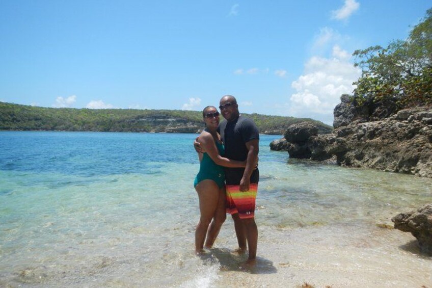 Two people standing in shallow water with a rocky shoreline and clear blue water in the background. 4
