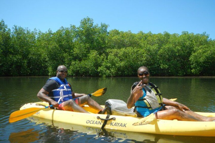 Two people kayaking on a yellow kayak with 'OCEAN KAYAK' written on it, surrounded by a dense green forest. 5