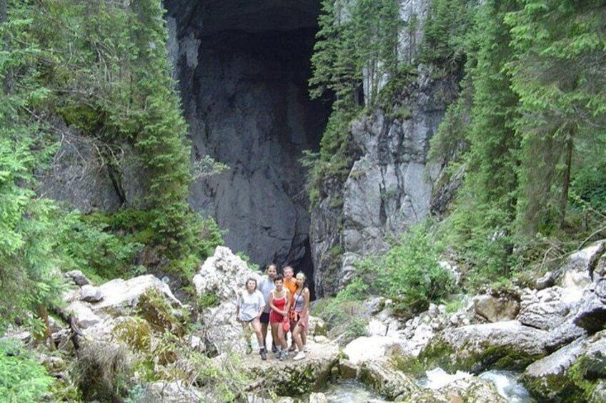 A group of people standing on a rocky outcrop with a cave entrance in the background. 2