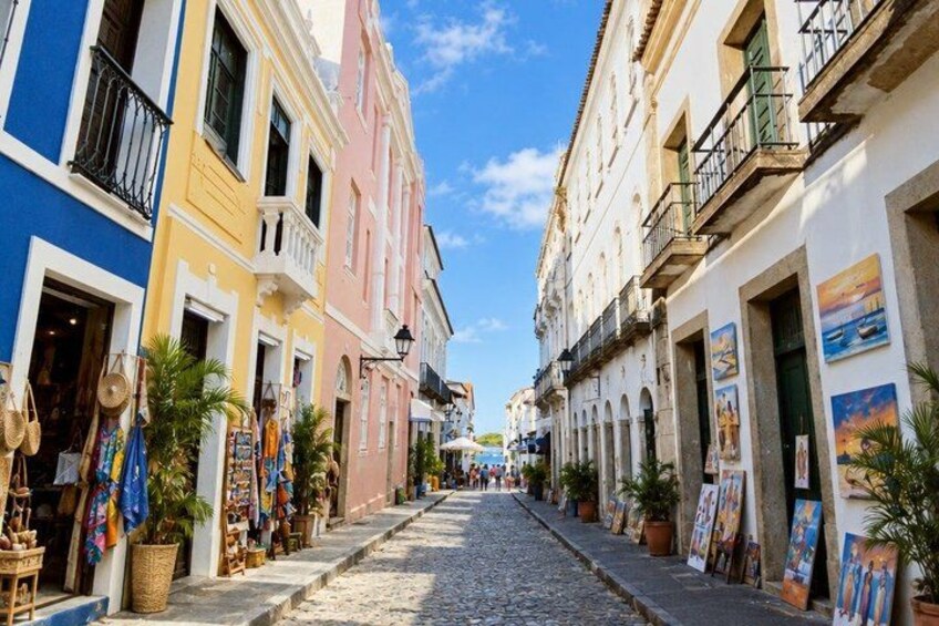 A cobblestone street lined with colorful buildings, some with balconies and outdoor displays. 2