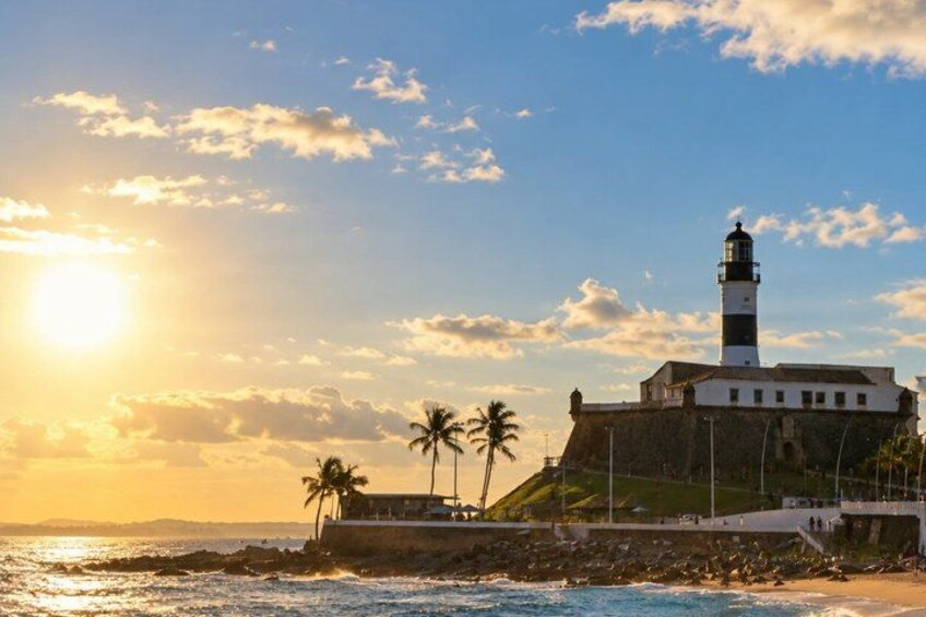 A lighthouse on a cliff, palm trees, and the ocean at sunset. 5