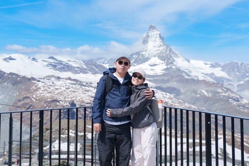 Two people standing on a balcony with a snow-covered mountain in the background. 2