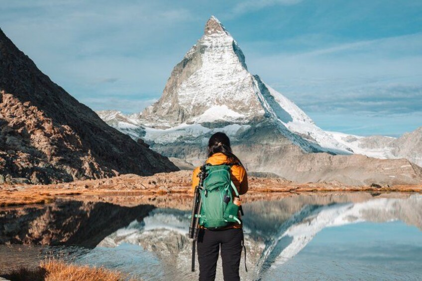 A person standing by a calm lake with a mountain in the background. 5