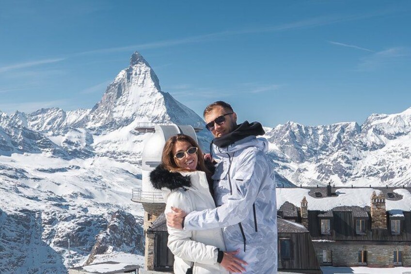 Two people embracing in a snowy mountainous area with a prominent peak in the background. 1