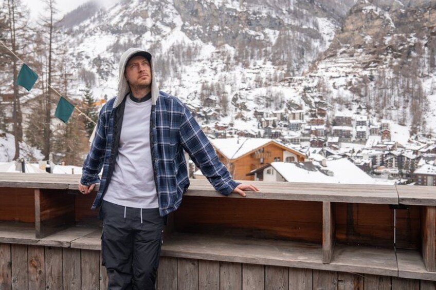 A person standing on a wooden platform with a snowy mountain village in the background. 4