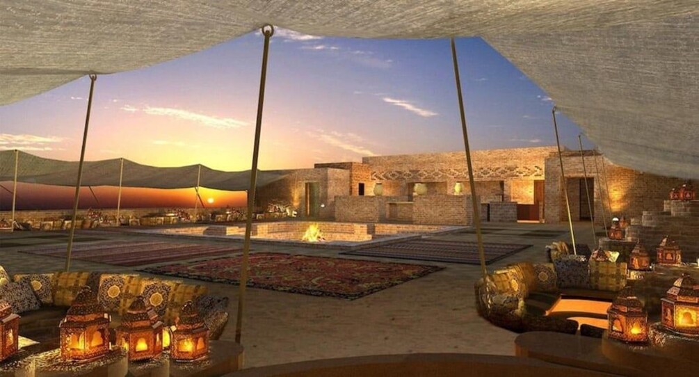 Une tente dans le désert offrant une vue sur le coucher de soleil, des lanternes traditionnelles et un bâtiment situé au loin. 4