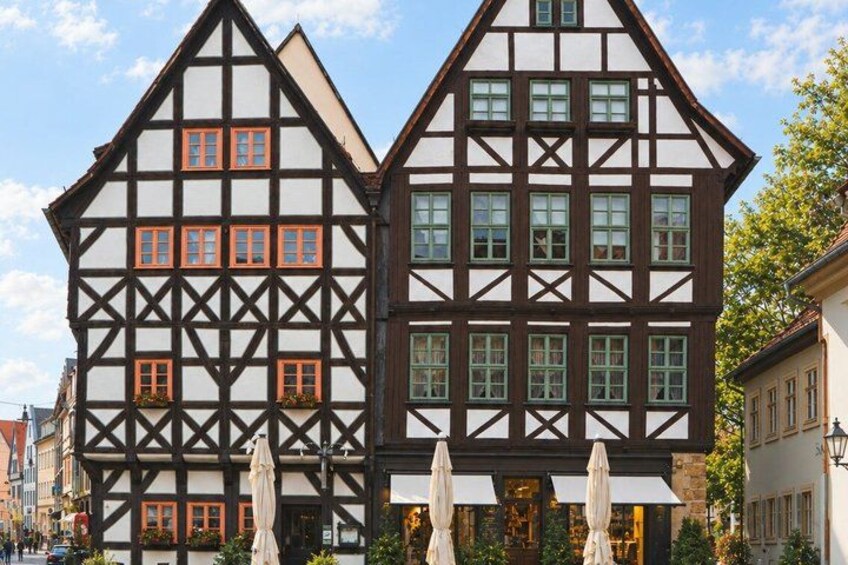 A traditional half-timbered building with a white facade and dark timber framing, accompanied by a smaller building with a similar architectural style. 3