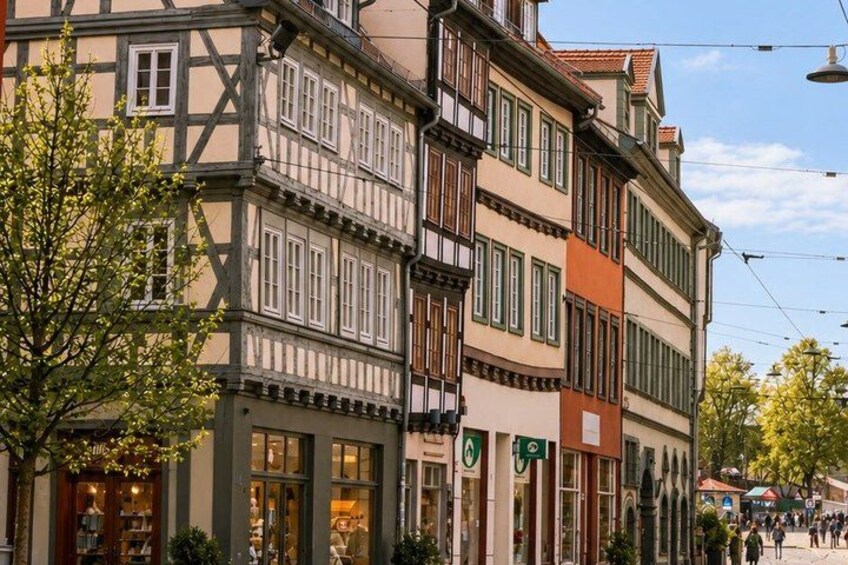 A street with traditional half-timbered buildings, a tree, and a tram line. 5