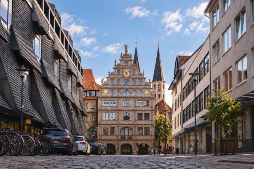 A cobblestone street with historic buildings, bicycles, and cars parked along the side. 5