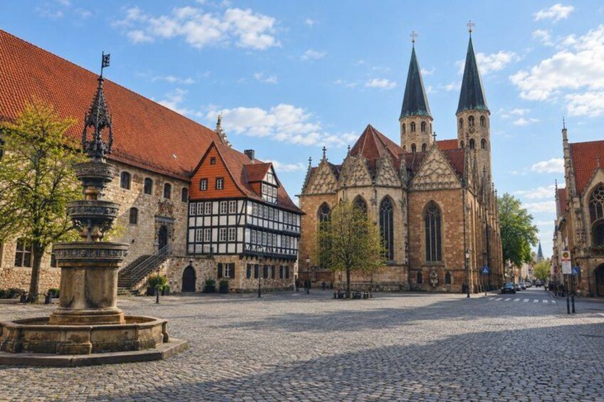 A cobblestone square with historic buildings, including a church with twin spires and a half-timbered house. 2
