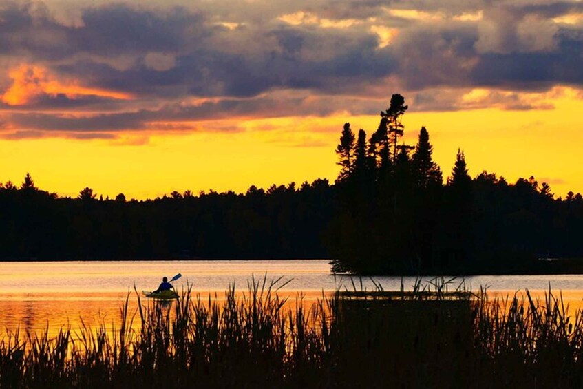 Un kayakista en un lago tranquilo al atardecer, con un bosque en el fondo. 4