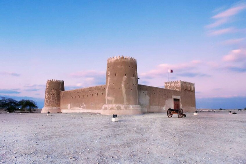 Una fortaleza grande e histórica con una torre central y un asta de bandera, con un cielo despejado de fondo. 1