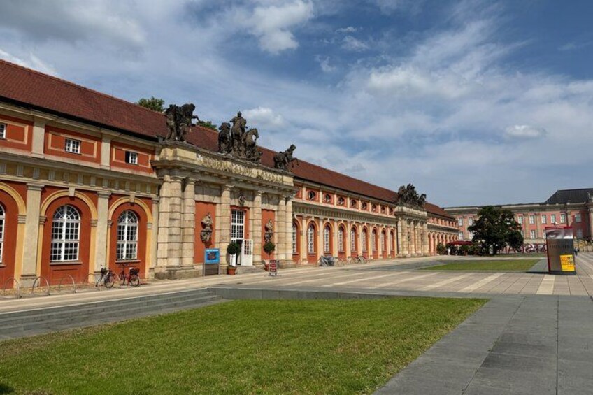 A historic building with red brick and yellow accents, large arched windows, and statues on the roof. 5