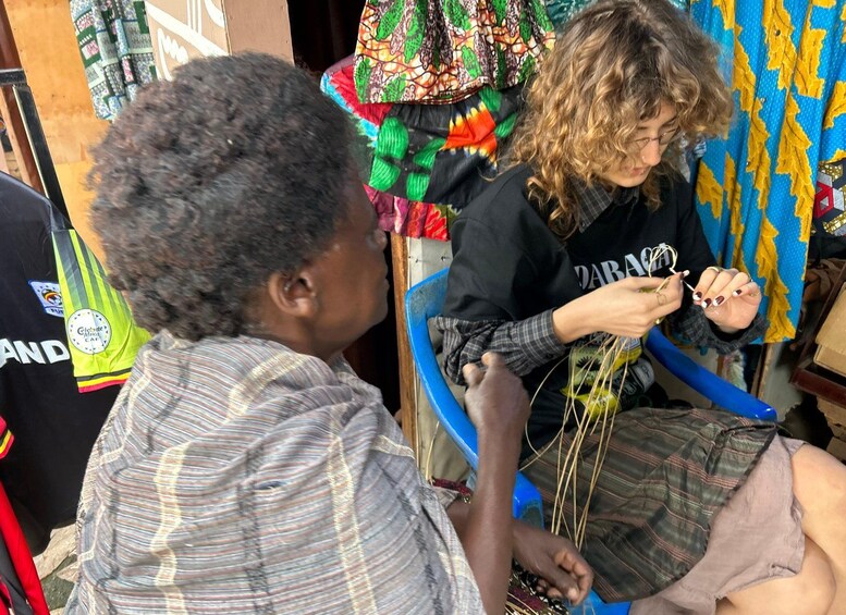 Dos personas realizando una actividad artesanal, quizás tejiendo o anudando, con telas y herramientas de colores en un ambiente informal. 2