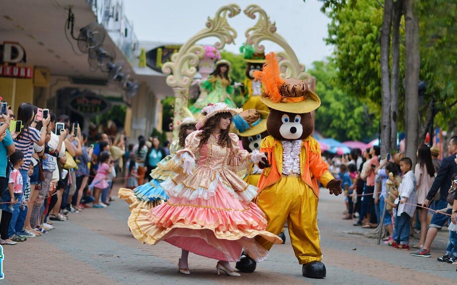 Un desfile con artistas en vestuarios coloridos, una multitud a lo largo de la calle y un arco decorativo al fondo. 3