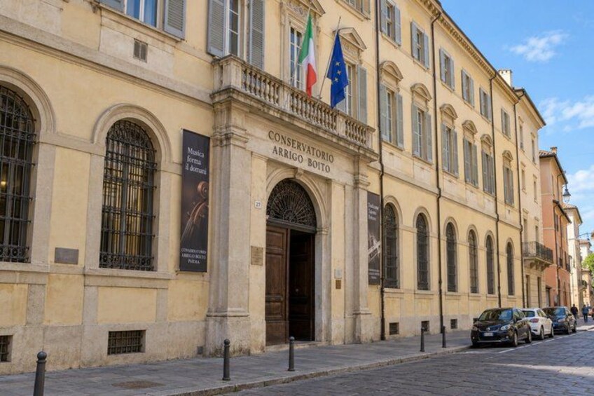 A historic building with arched windows and a sign reading 'CONSERVATORIO ARRIGO BOITO.' Flags of Italy and the European Union are displayed. 3