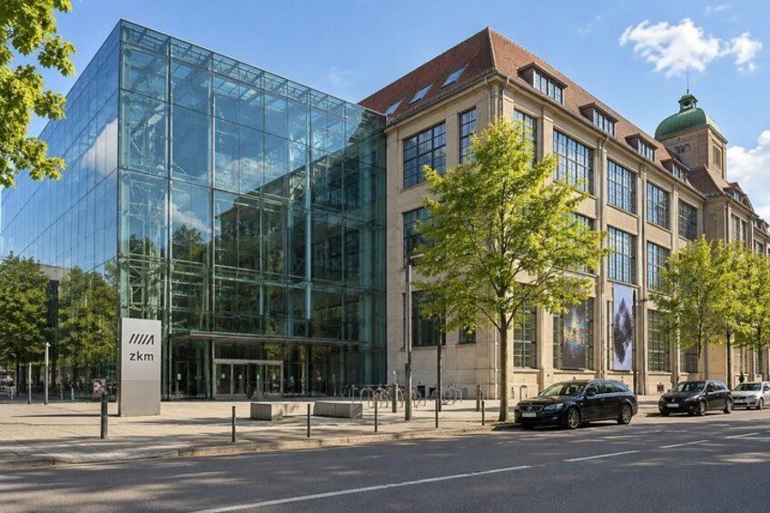 A modern glass building with a traditional brick structure, parked cars, and trees. 2