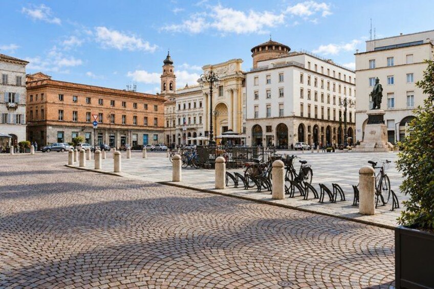 A cobblestone square with historic buildings, a clock tower, and a statue. 4