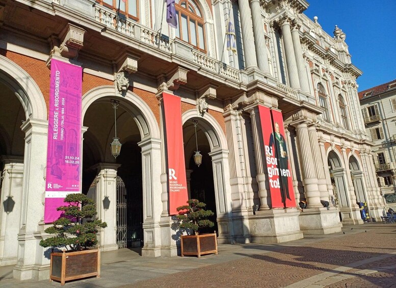 Un edificio histórico con arquitectura ornamentada, incluyendo columnas y arcos, y pancartas anunciando un evento. 1
