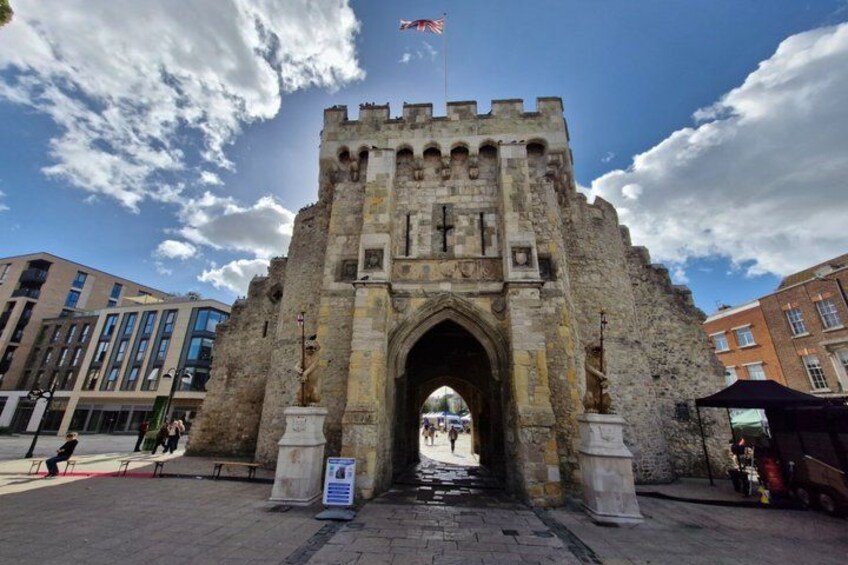A historic stone archway with a flag, surrounded by modern buildings. 4