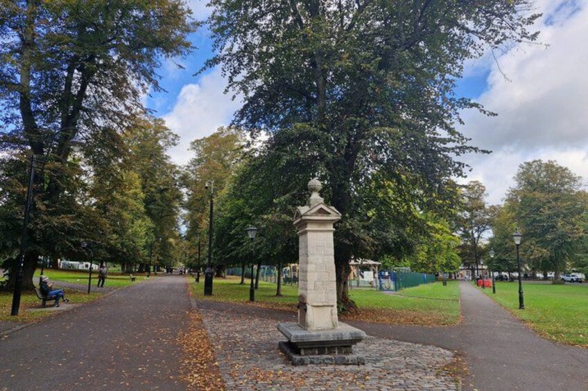A park with a paved path, a stone monument, and trees. 3