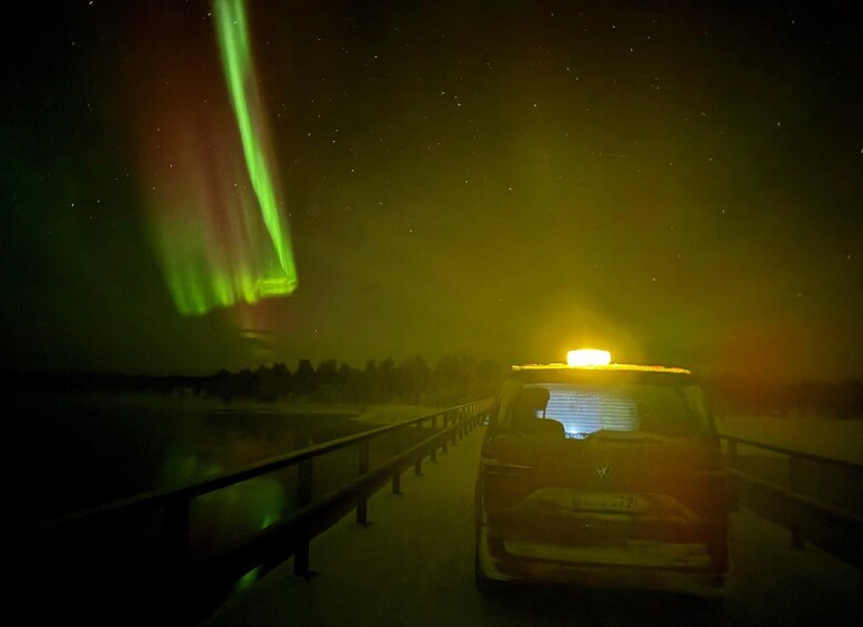 A car driving on a highway at night with green lights in the sky. 5