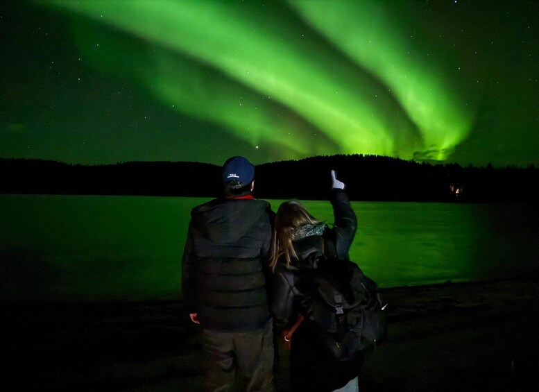 Two people observing the Northern Lights over a body of water. 1
