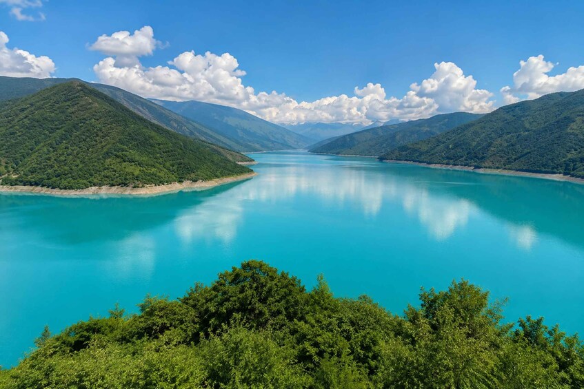 A turquoise lake surrounded by lush green hills and mountains under a clear blue sky. 5