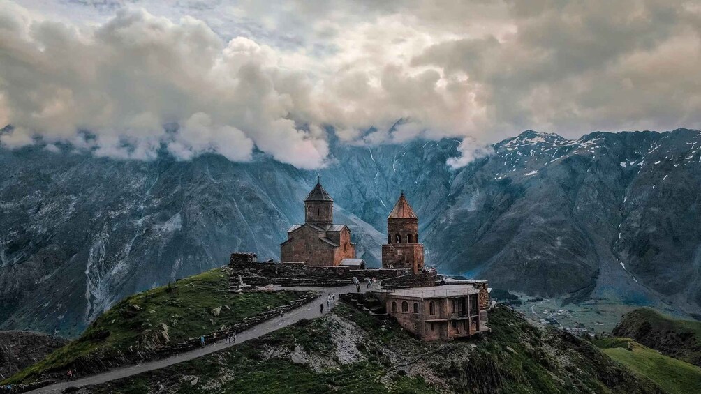 A historic church with two bell towers on a mountain peak, surrounded by rugged terrain and snow-capped mountains. 2