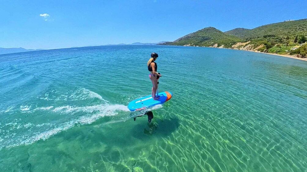 A person paddleboarding on clear turquoise water with a mountainous coastline in the background. 5
