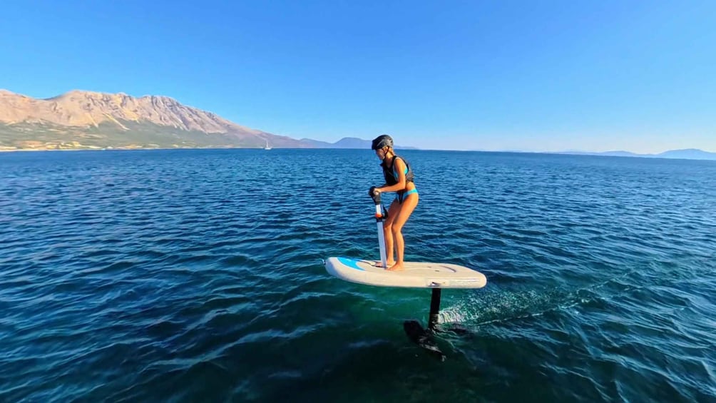 A person paddleboarding on a calm sea with mountains in the background. 4