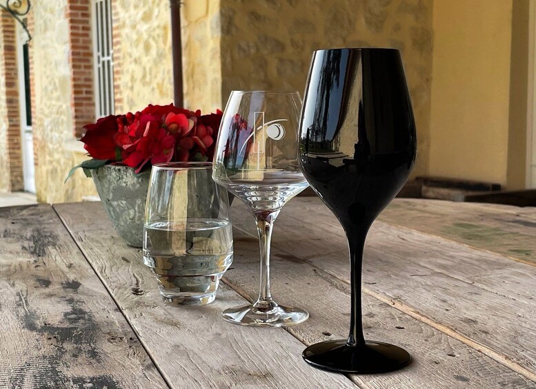 Three wine glasses on a wooden table with a vase of red flowers in the background. 1