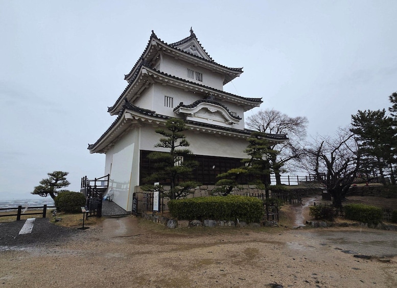 Edificio japonés tradicional con techo de tejas y base de piedra, rodeado de árboles y un camino de grava. 4