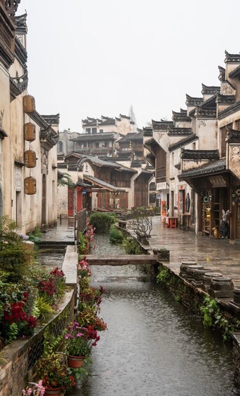 Une cour traditionnelle chinoise, avec un étroit canal d’eau, entourée de bâtiments aux toits richement décorés et illuminés de lanternes suspendues. 3